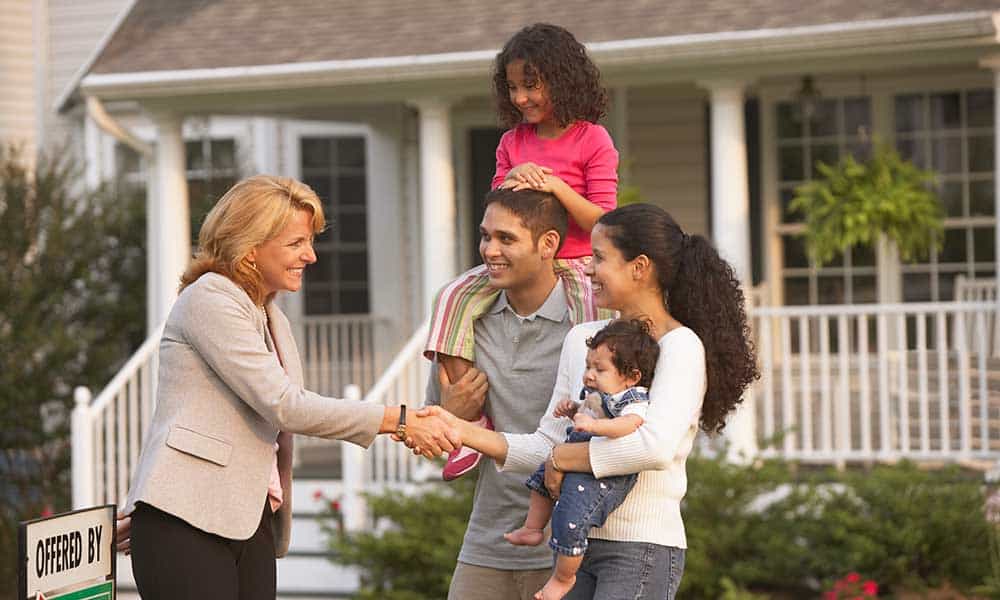 family of 4 shaking hands with real estate agent in front of house