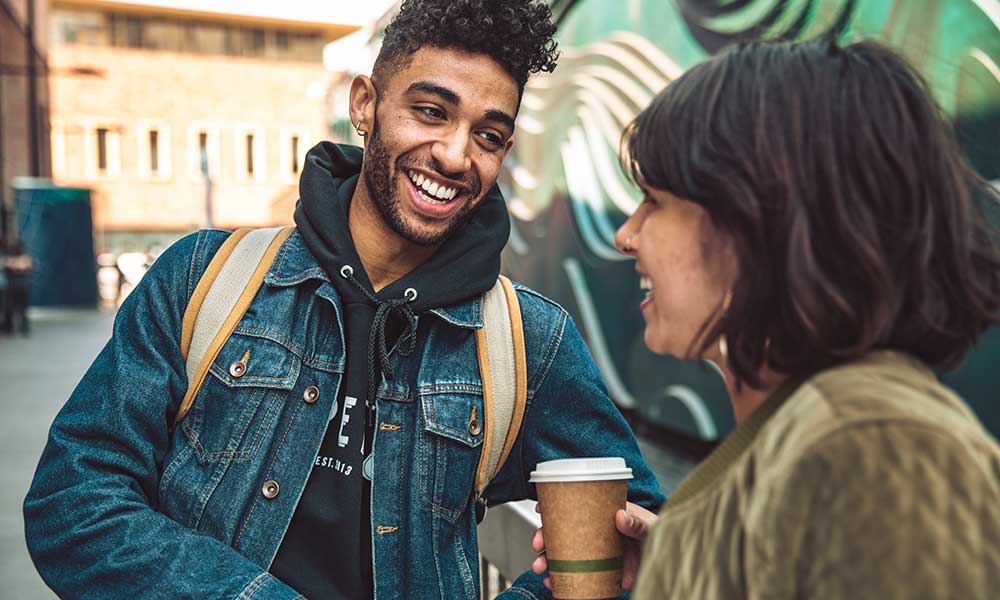 Happy young man and woman with coffee talking in the city
