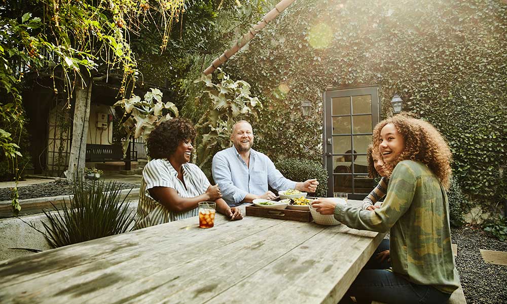 Laughing family sharing meal at picnic table in backyard 