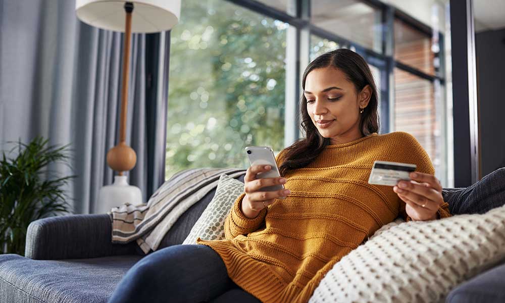 young woman using her cellphone and credit card while relaxing on a couch at home