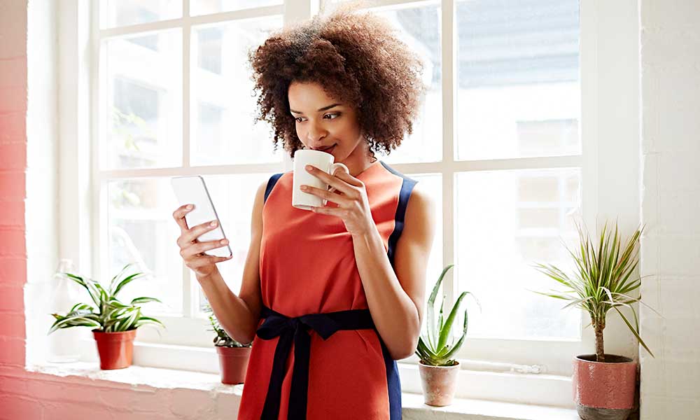 Woman drinking coffee while looking at smartphone