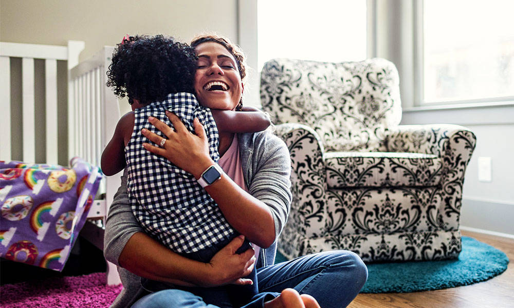 Young daughter giving her mother a hug on the bedroom floor.