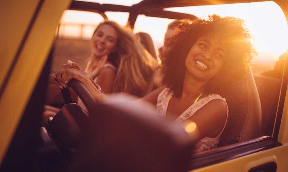 two female friends smiling in car on a road trip at sunset