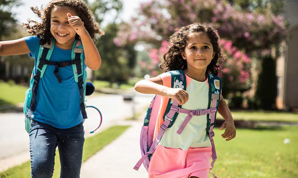 two young girls running outside wearing backpacks