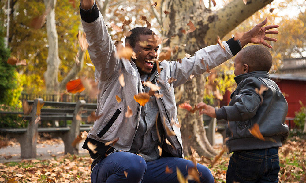 father embracing young son while leaves fall in yard