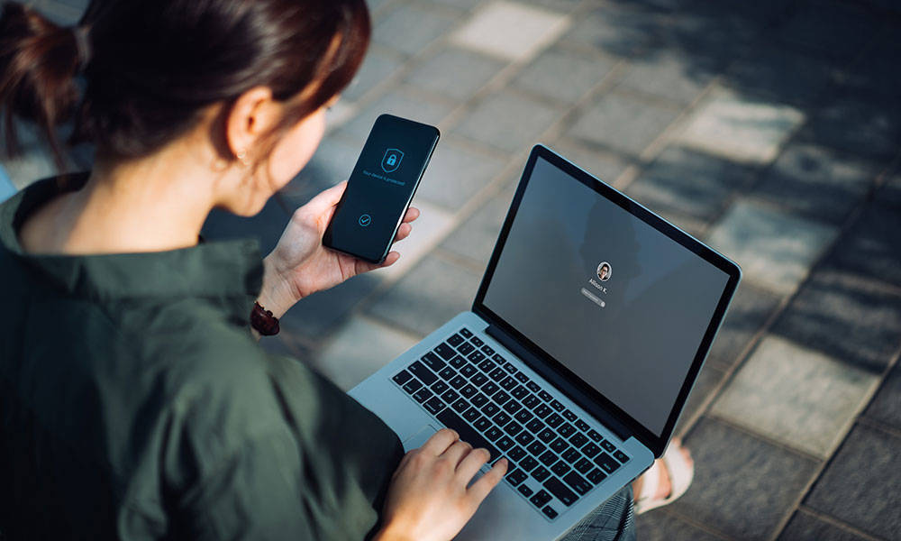 young woman authenticating login to her laptop with smartphone