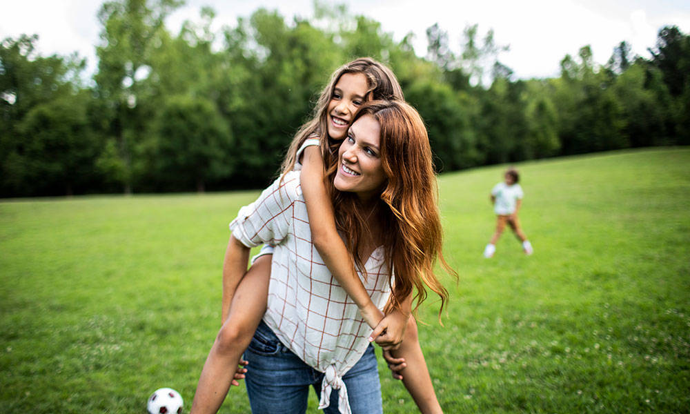 daughter riding on mothers shoulders at park