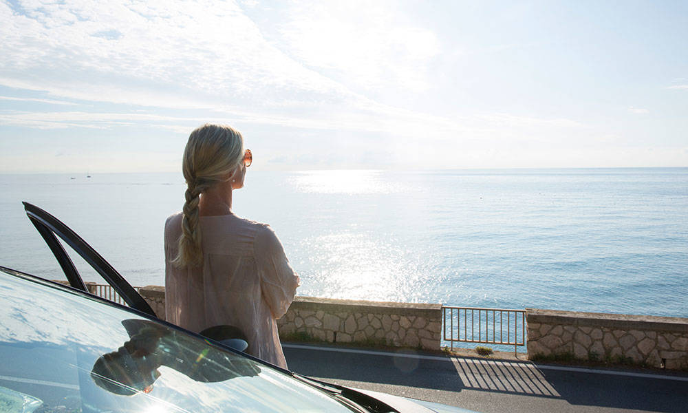 woman outside of her car looking out into the ocean