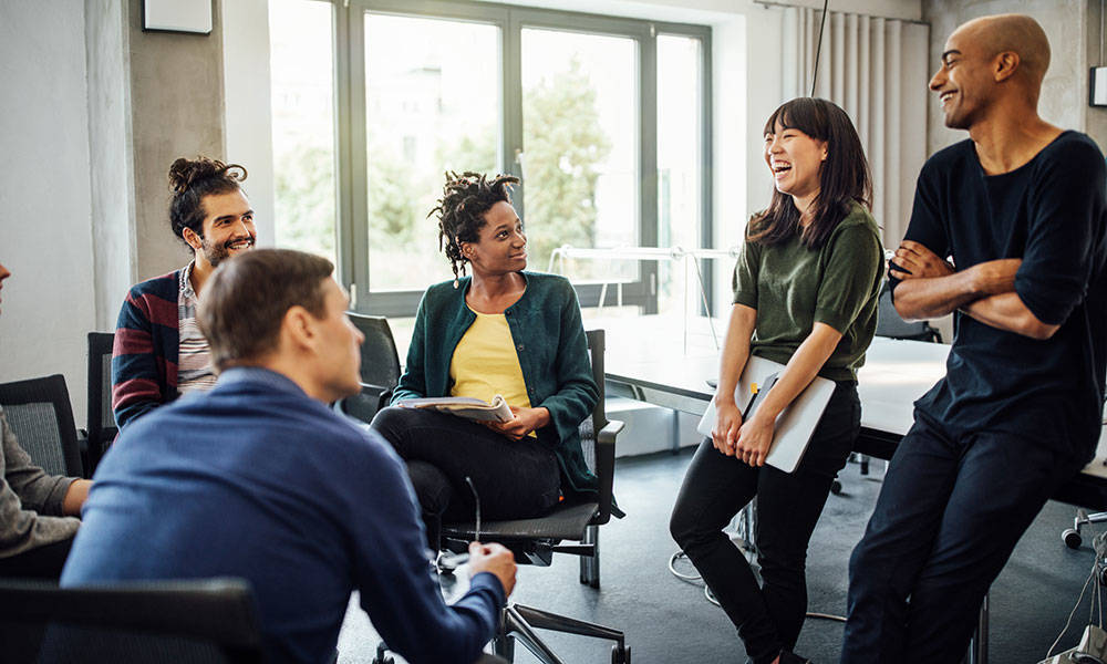 work colleagues looking at cheerful businesswoman holding laptop in meeting