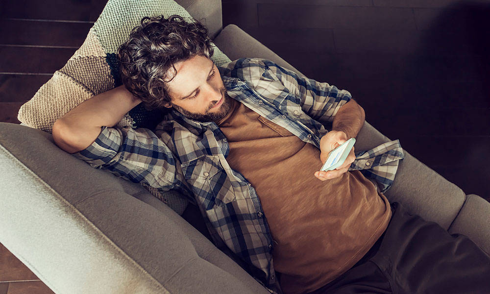 man relaxing on couch on his smartphone