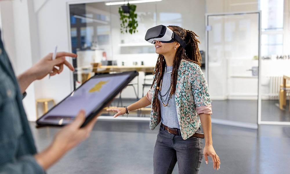 young woman wearing virtual reality headset by male colleague using digital tablet