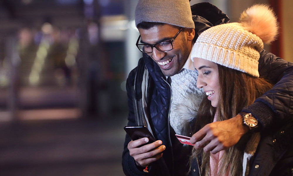 young couple at night, paying for something on phone with card