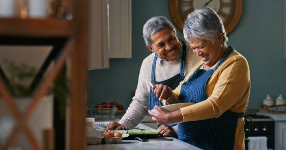 Elderly couple smiling and cooking in the kitchen while enjoying retirement.