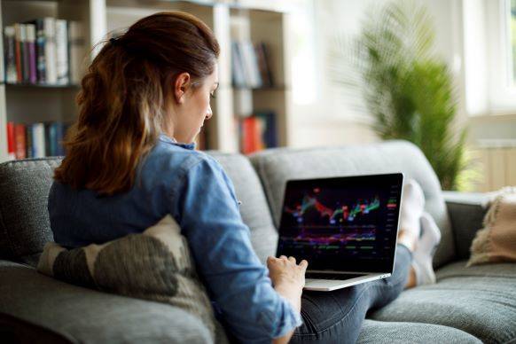 Woman reviewing stock market and investments on laptop from the couch at home.