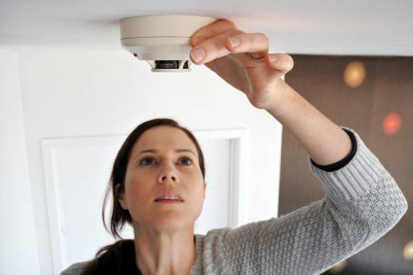Woman checking smoke detector batteries on ceiling in her home.