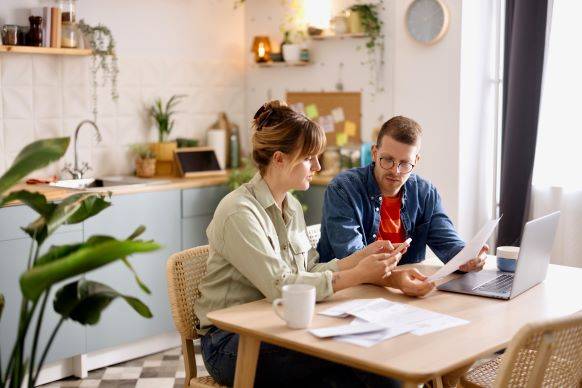Man and woman sitting at kitchen table reviewing documents and discussing finances.