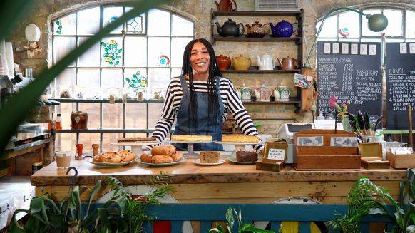 Woman smiling towards the camera and standing at the counter of her small business shop