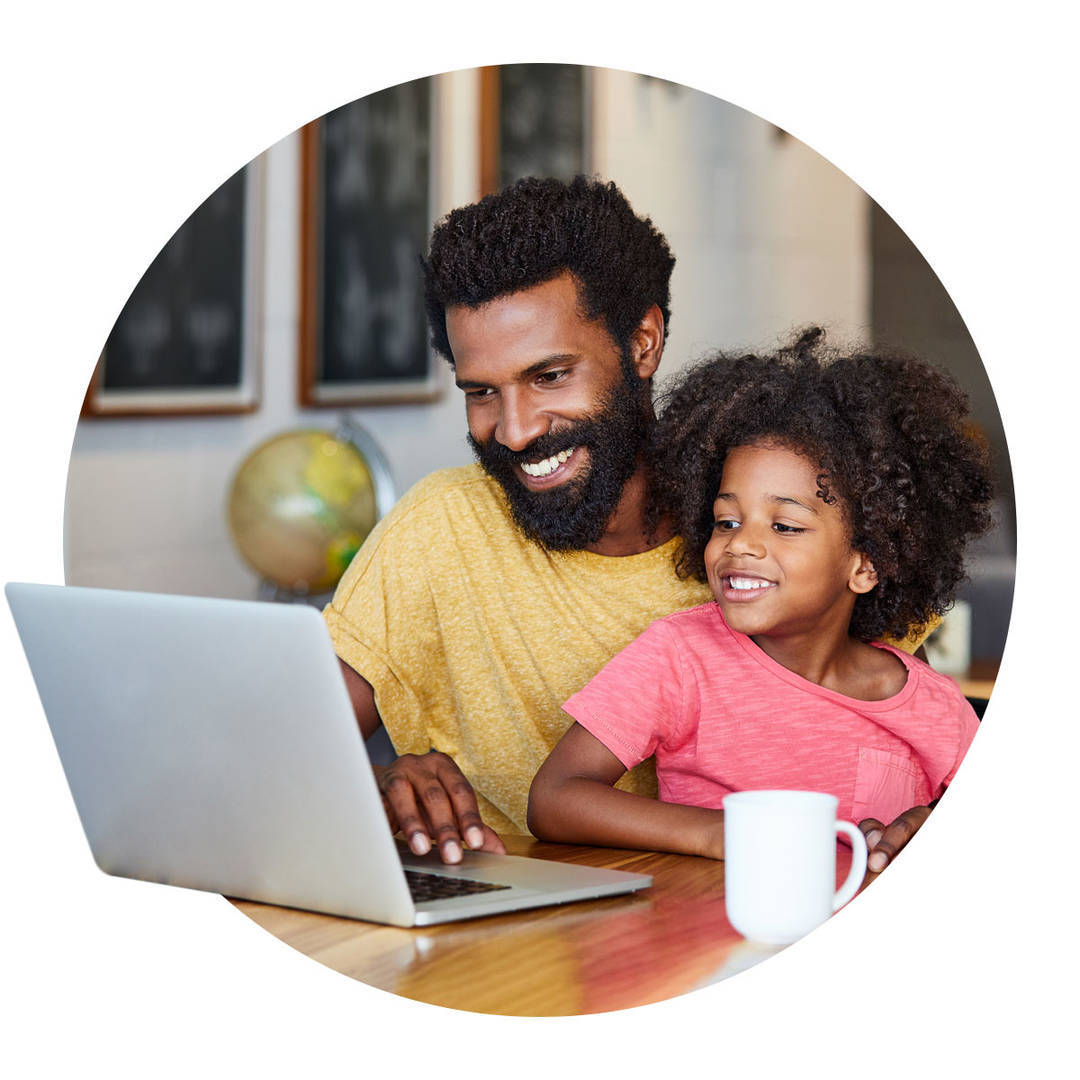 Cheerful young father and son browsing for cars on a laptop together while being seated at a table in their home.