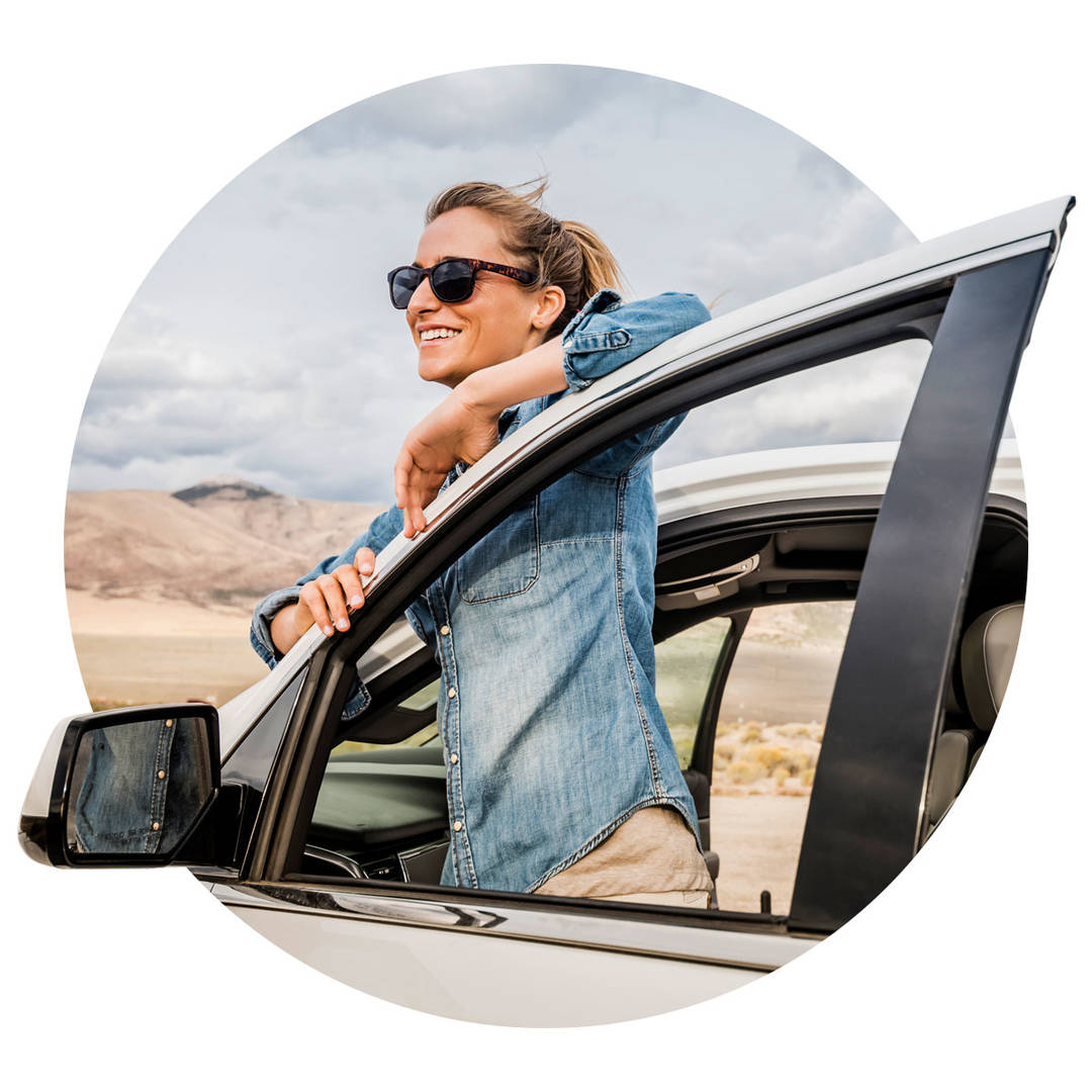 Woman wearing sunglasses steps out of the driver's side of the car to take a look at the beautiful scenery.