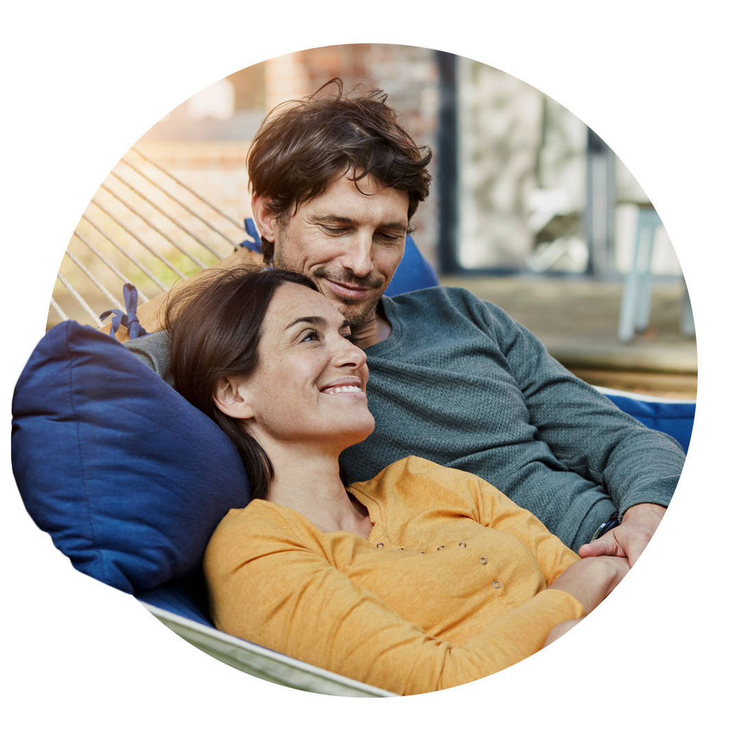 Smiling couple lying in hammock in garden of their home