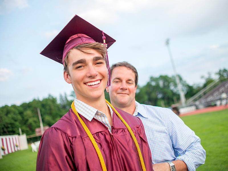 High School senior being hugged by father at graduation ceremony.