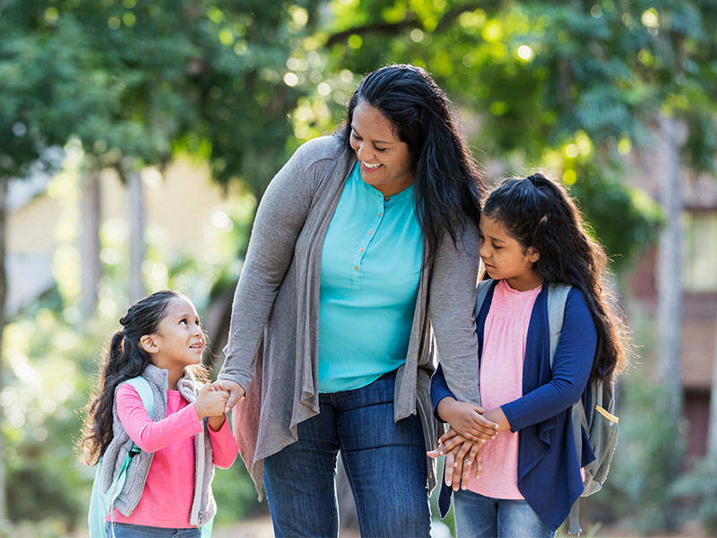 Mother taking her two young girls to school on a beautiful sunny day.
