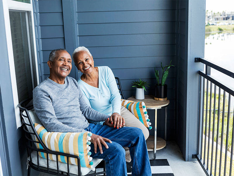 Senior couple relaxing and holding hands on porch of their apartment.