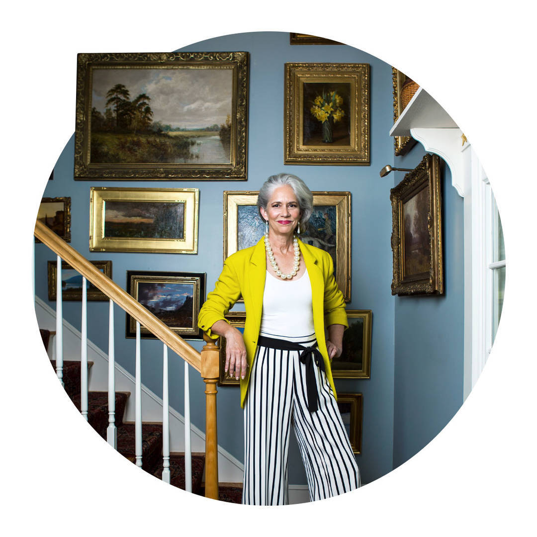 A female collector standing in a staircase with golden framed oil paintings on the wall.