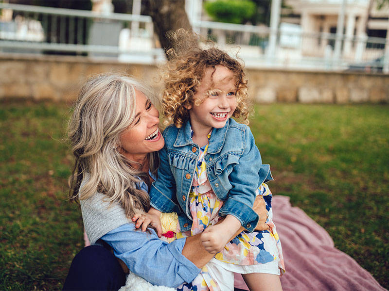 Loving grandmother and little granddaughter embracing, having fun and playing together in park.