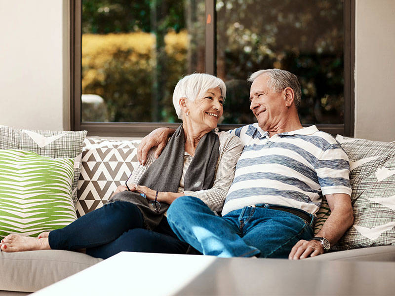 Senior couple relaxing together on a sofa outside on their back patio.