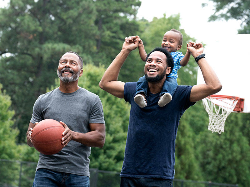 Grandfather, young father, and toddler happily playing basketball.