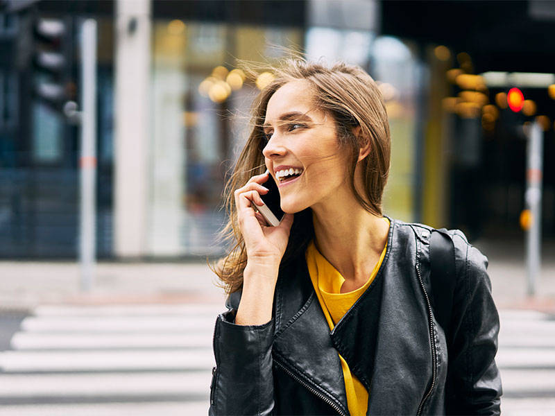 Laughing woman crossing the street while talking on the phone.