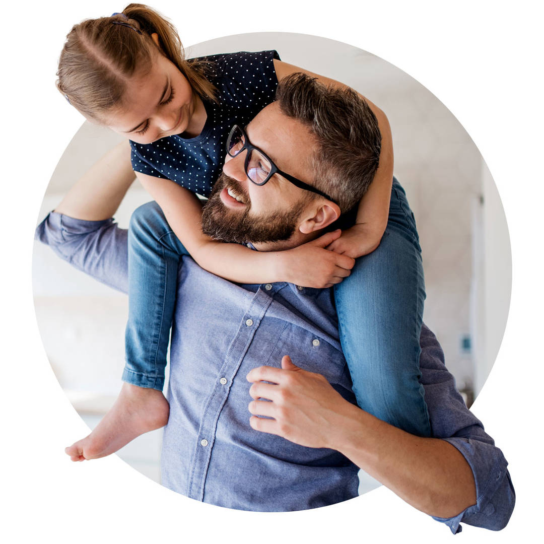 Mature father giving piggyback ride to small daughter indoors at home.