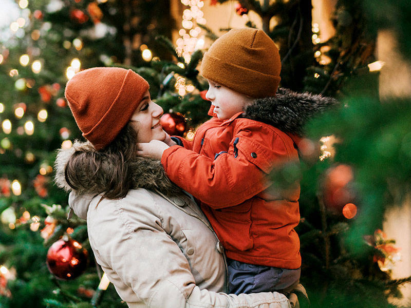 Mother holding young son, who is bundled up in a heavy jacket, as they walk into a holiday store