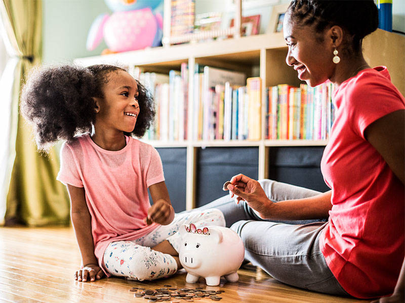 Mother teaches her young daughter how to save using a piggy bank