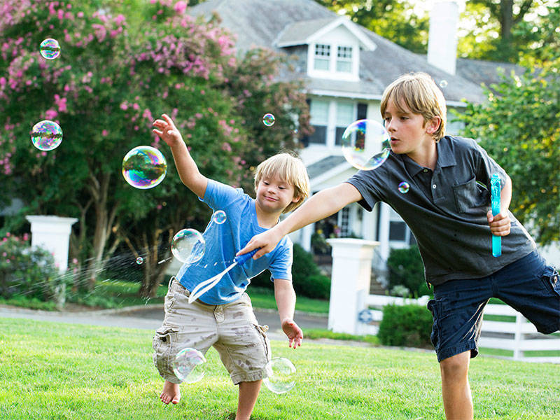 A child with special needs playing with his brother who is blowing bubbles in the back yard.