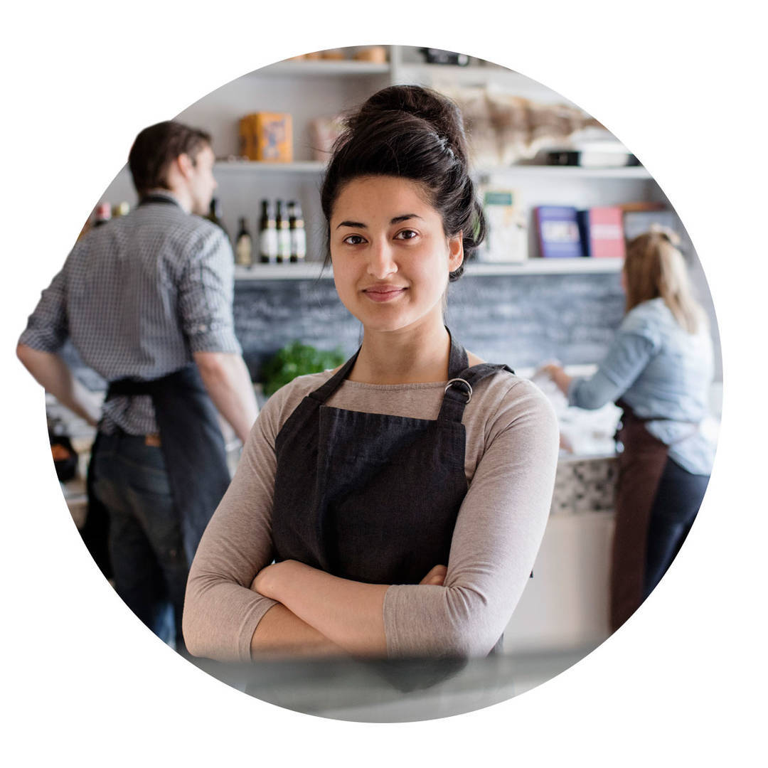 Confident small business owner standing at the restaurant counter while her two employees are diligently working behind.